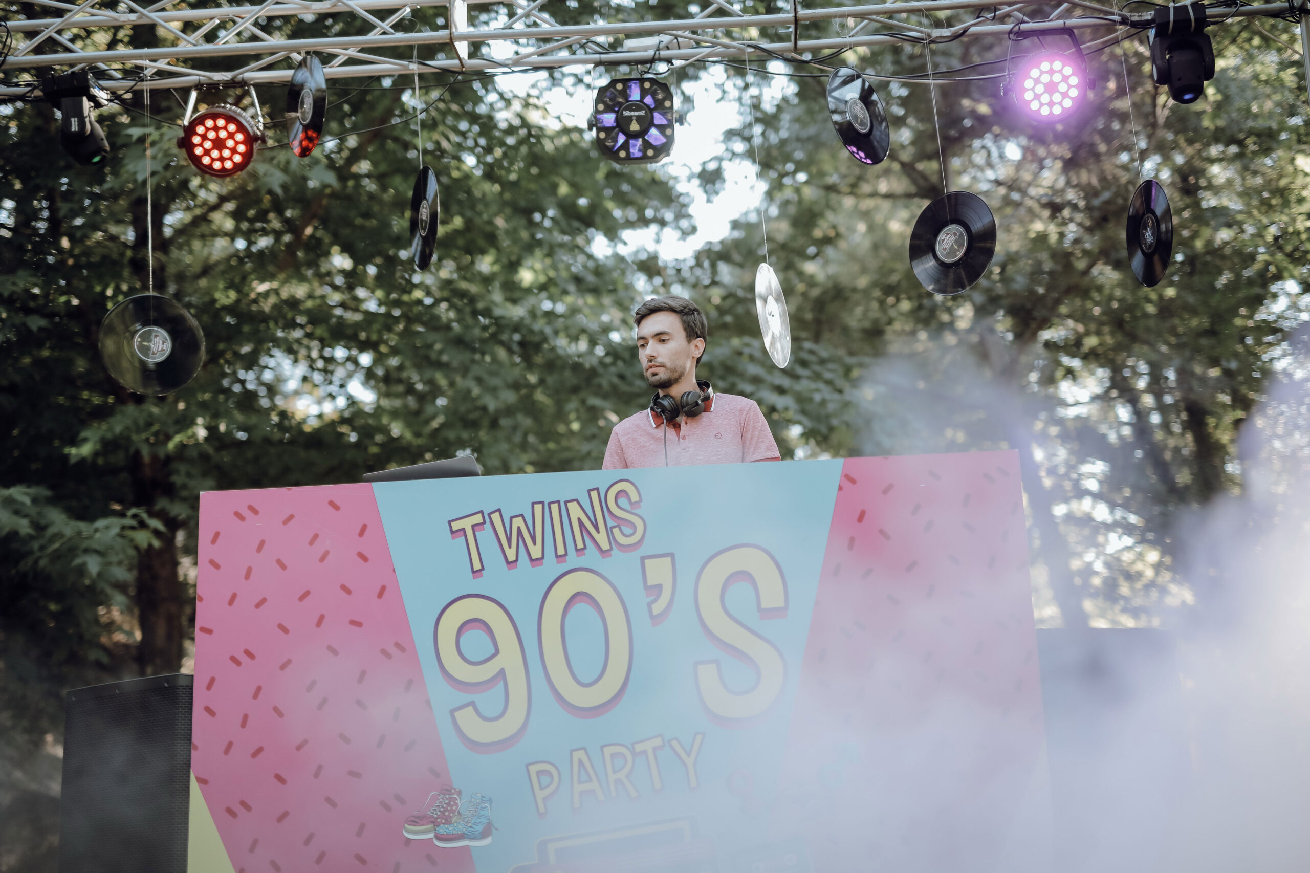 Fotografia de um DJ a trabalhar em sua box para o evento Twins 90's Party, cercado de discos e luzes.